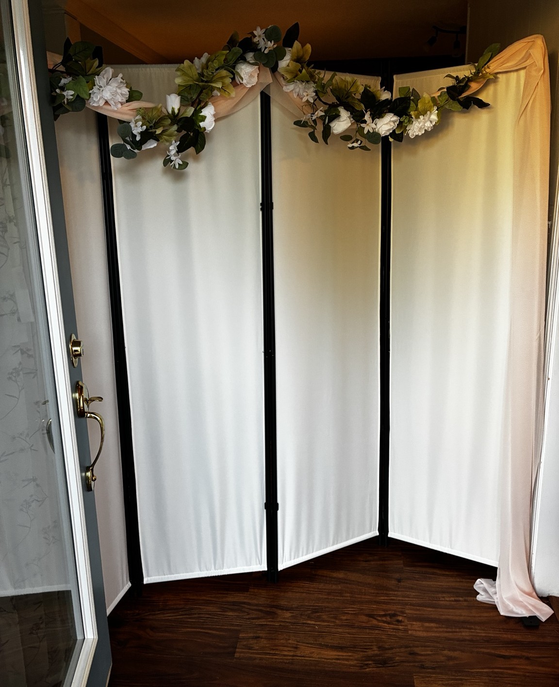 Folding screen just inside the front door, draped in blush fabric and topped with white flowers and greenery